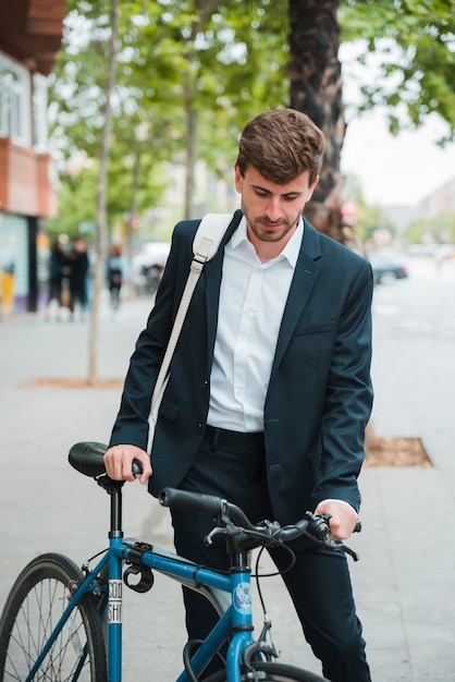 Młody biznesmen z jego plecak pozycją z bicyklem na ulicie