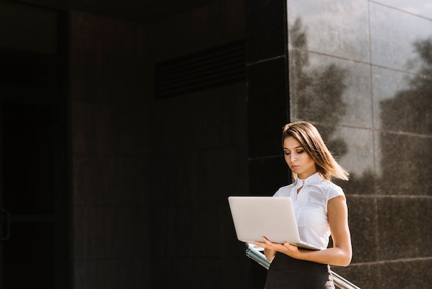 Bezpłatne zdjęcie młody bizneswoman używa laptop pozycję na zewnątrz budynku
