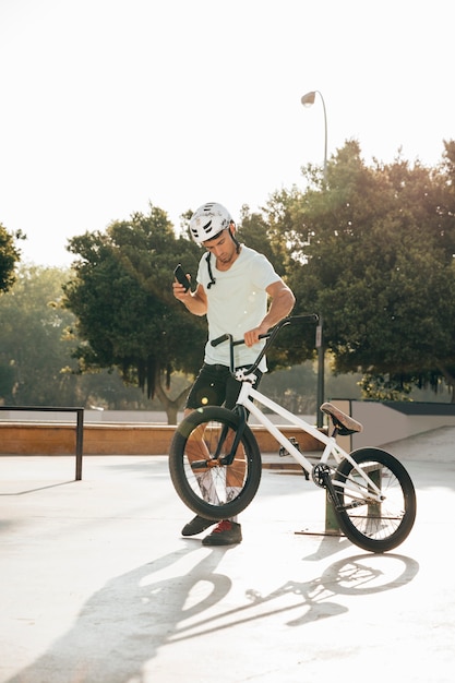 Bezpłatne zdjęcie młody bmx jeździec patrzeje jego telefonu strzał w dal