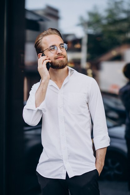 Młody brodaty mężczyzna korzystający z telefonu i idący ulicą