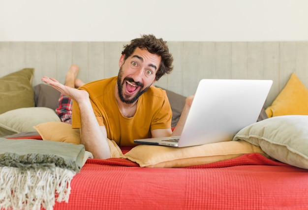 Młody brodaty mężczyzna na łóżku z laptopem