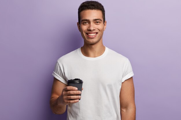 Młody brunet mężczyzna ubrany w białą koszulkę i trzymając filiżankę kawy