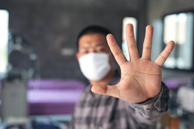 Młody chłopak bawi maskę i robi przerwy ręki znakowi odizolowywającemu przy szpitalem.