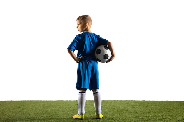 Bezpłatne zdjęcie młody chłopak jako piłkarz lub piłkarz w stroju sportowym, stojący z piłką jak zwycięzca, najlepszy napastnik lub bramkarz na białej ścianie. sprawny chłopiec grający w akcji, ruchu, ruchu w grze.
