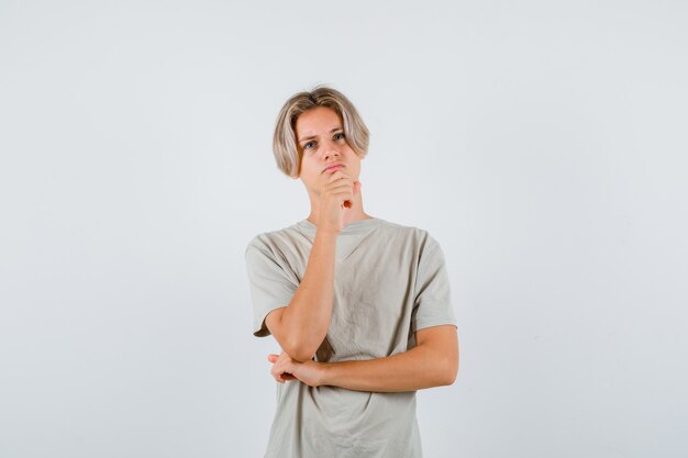 Młody chłopak teen w t-shirt, trzymając rękę na brodzie, patrząc w górę i patrząc zamyślony, widok z przodu.