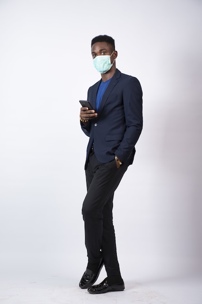 Młody czarny biznesmen ubrany w garnitur i maskę na twarzy, używający swojego telefonu