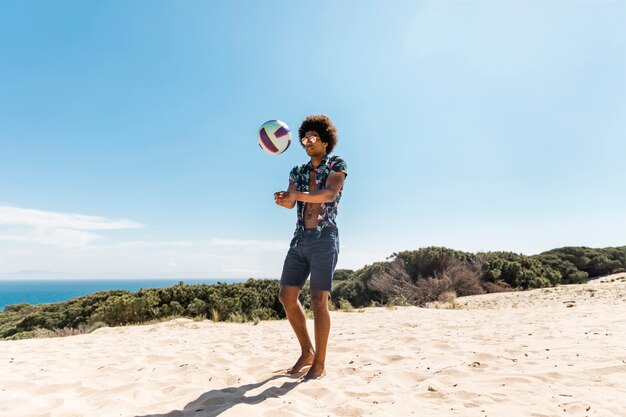 Młody człowiek African American rzuca piłkę na plaży