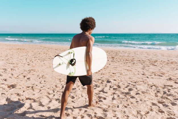 Młody człowiek African American z deska surfingowa na plaży