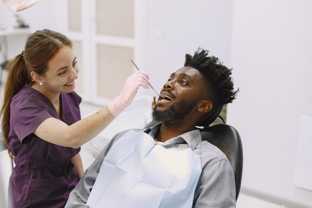 Młody człowiek afroamerykanin. Facet odwiedzający gabinet dentystyczny w celu zapobiegania jamy ustnej. Mężczyzna i znany lekarz podczas kontroli zębów.