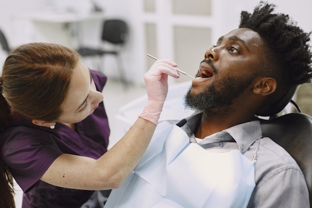 Młody człowiek afroamerykanin. Facet odwiedzający gabinet dentystyczny w celu zapobiegania jamy ustnej. Mężczyzna i znany lekarz podczas kontroli zębów.