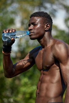 Młody człowiek afroamerykanin pije wodę podczas treningu w parku na boisku sportowym, koncepcja treningu na świeżym powietrzu, crossfit.