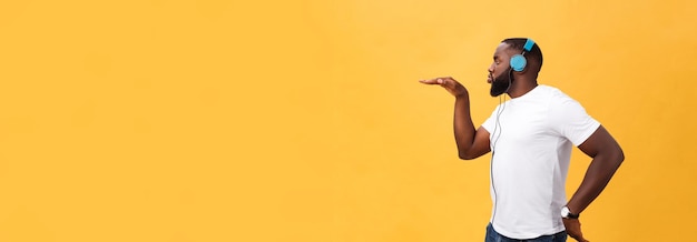Bezpłatne zdjęcie młody człowiek afroamerykanów noszenie słuchawek i cieszyć się tańcem muzyki na żółtym tle złota