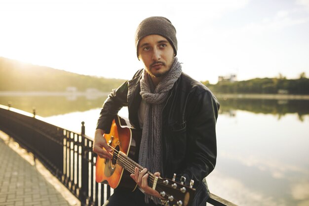 Młody człowiek bawić się na gitarze przy jeziorem
