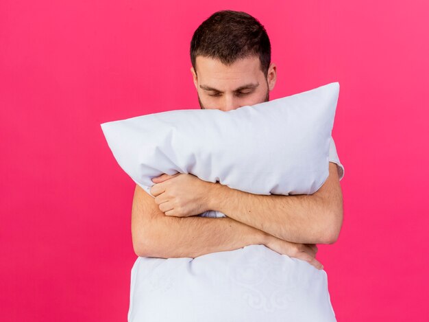 młody człowiek chory przytulił poduszkę na różowym tle