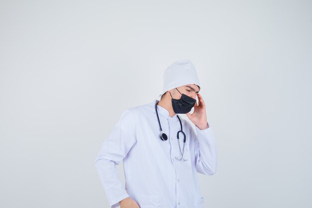 Młody człowiek cierpiący na ból głowy w białym mundurze, masce i bolesny wygląd. przedni widok.