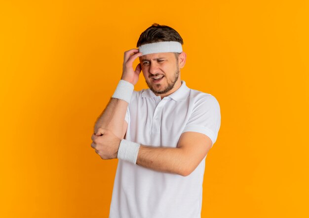 Młody człowiek fitness w białej koszuli z pałąkiem na głowę patrząc na bok mylić stojąc na pomarańczowym tle