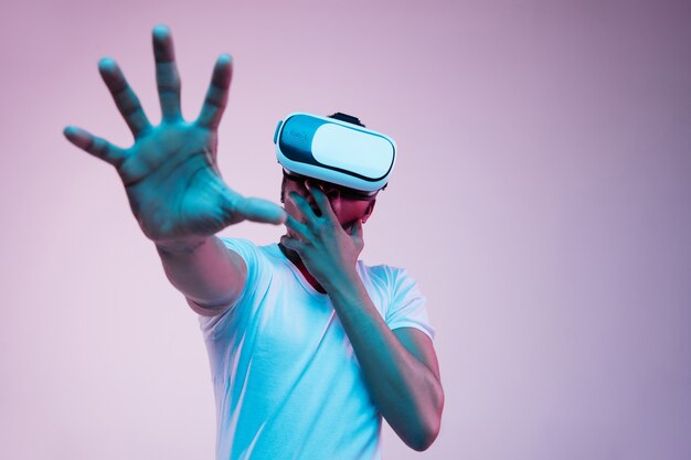 Młody człowiek gra w okularach VR w świetle neonu na gradiencie