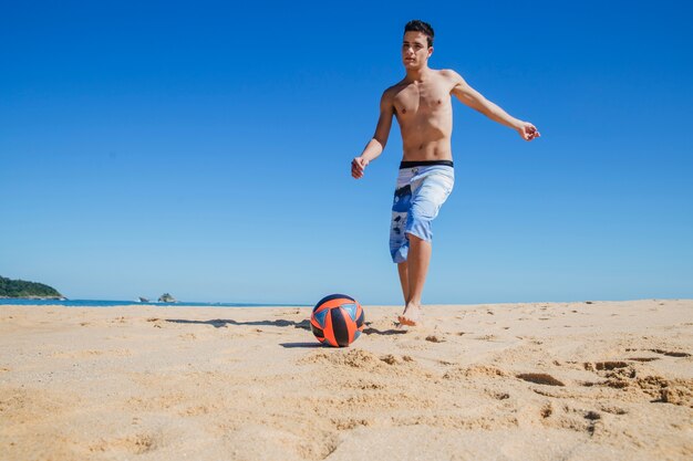 Młody człowiek gra w piłkę nożną na plaży