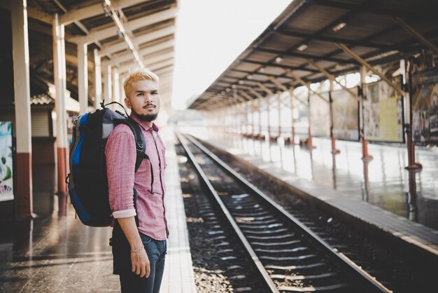 Młody człowiek hipster czeka na platformie stacji z plecakiem. Koncepcja podróży.