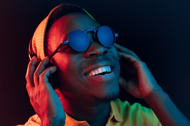 młody człowiek hipster słuchanie muzyki w słuchawkach w czarnym studio z neonów.