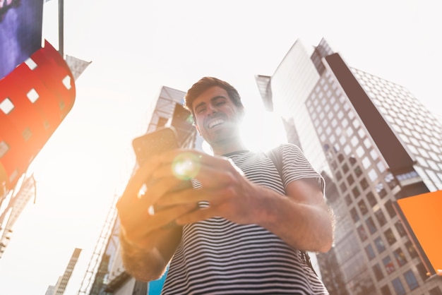 Młody człowiek ono uśmiecha się podczas gdy używać jego smartphone