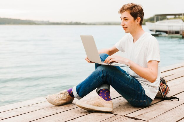 Młody człowiek pisze na laptopie nad jeziorem