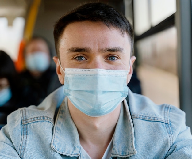 Bezpłatne zdjęcie młody człowiek podróżujący autobusem miejskim w masce chirurgicznej