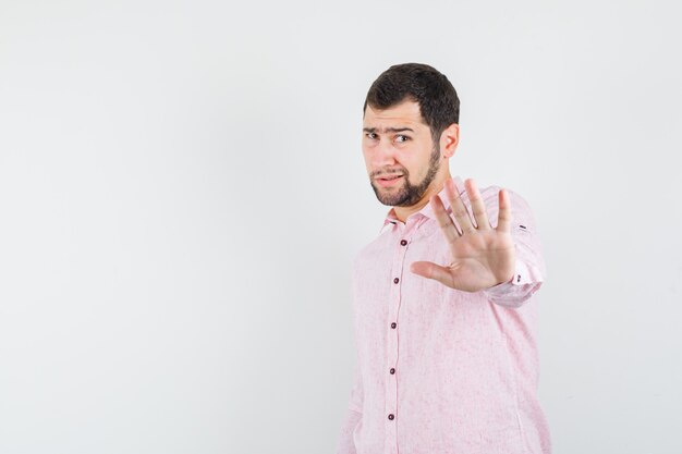 Młody człowiek pokazujący gest odmowy w różowej koszuli i wyglądający na zirytowanego