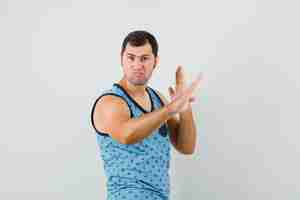 Bezpłatne zdjęcie młody człowiek pokazuje gest chop karate w niebieskim podkoszulku i wygląda pewnie. przedni widok.