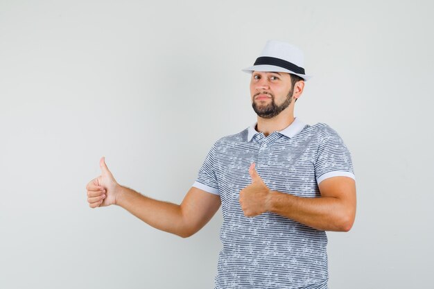 Młody człowiek pokazuje kciuk w pasiastej koszulce, kapeluszu i cieszy się. przedni widok.