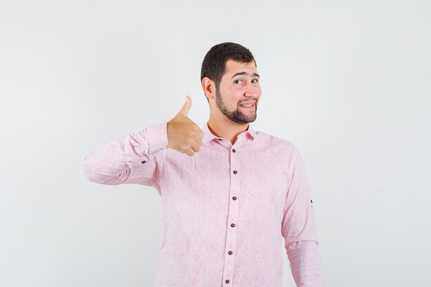 Młody człowiek pokazuje kciuk w różowej koszuli i szuka zadowolony