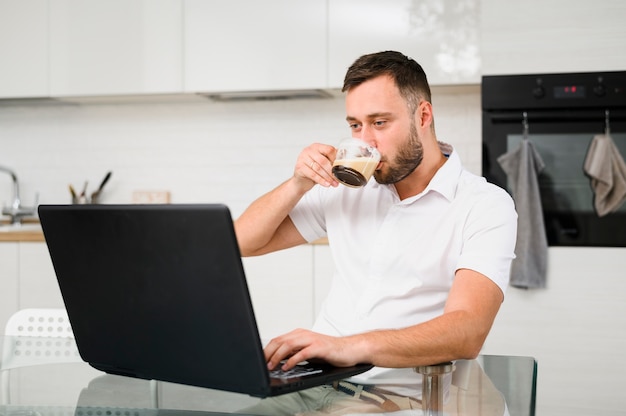 Młody człowiek popija kawę podczas gdy patrzejący laptop