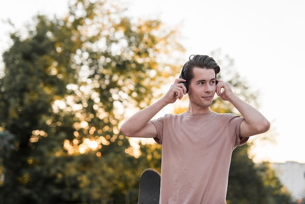 Bezpłatne zdjęcie młody człowiek pozuje z deskorolka i słuchawkami
