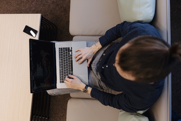 Młody człowiek pracuje na laptopie podczas gdy siedzący na kanapie w biurze