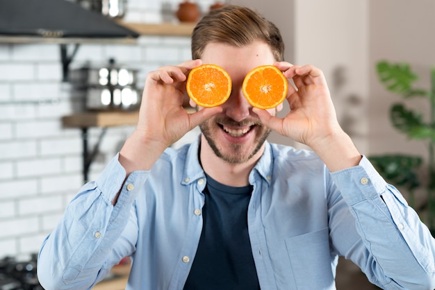Bezpłatne zdjęcie młody człowiek robi zabawie z dwa pomarańczami ciąć w domu