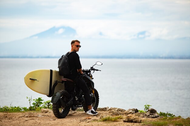 Młody człowiek siedzi na motocyklu z deską surfingową