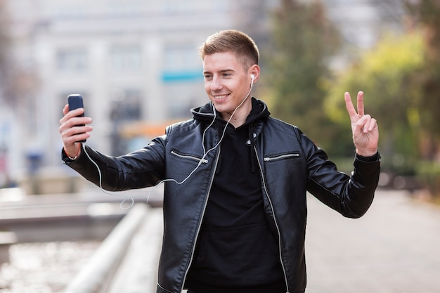 Młody człowiek słucha muzyka na słuchawkach podczas gdy brać selfie