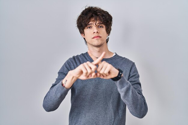Bezpłatne zdjęcie młody człowiek stojący nad wyrazem odrzucenia na białym tle, krzyżujący palce, robiący znak ujemny