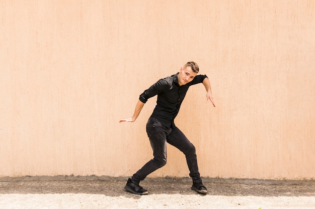 Młody człowiek tańczy hip-hop na beżowej ścianie