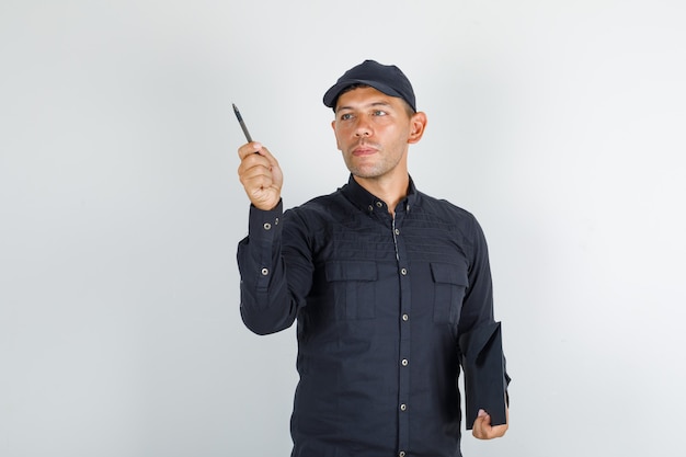 Młody człowiek trzyma pióro i folder w czarnej koszuli z czapką