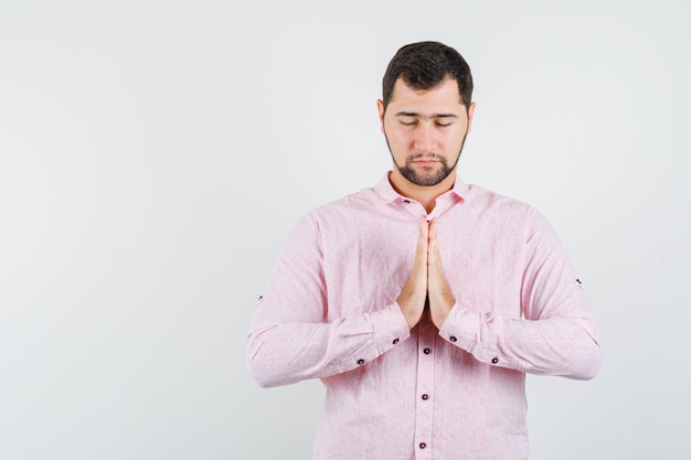 Młody człowiek trzymając się za ręce w geście modlitwy w różowej koszuli i patrząc spokojnie