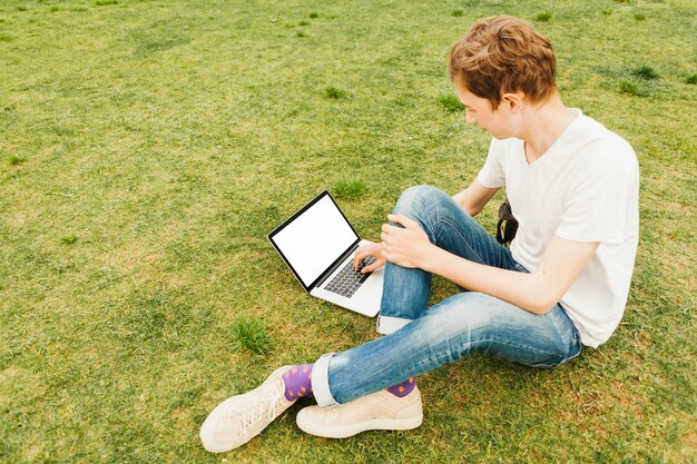 Młody człowiek używa laptop na zielonej trawie