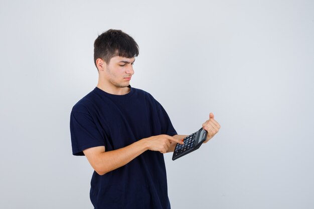 Młody człowiek w czarnej koszulce dokonywania obliczeń na kalkulatorze i patrząc zajęty, widok z przodu.