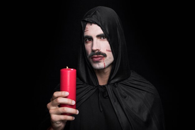 Młody człowiek w czarnym Halloweenowym kostiumu pozuje w studiu z świeczką