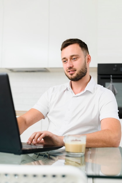 Młody człowiek w kuchni pracuje na laptopie