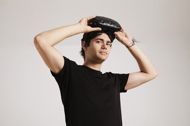 Młody człowiek w nieoznakowanej czarnej koszulce zakładającej zestaw VR na białym tle