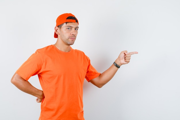 Młody człowiek w pomarańczowej koszulce i czapce, wskazując na bok i patrząc poważnie