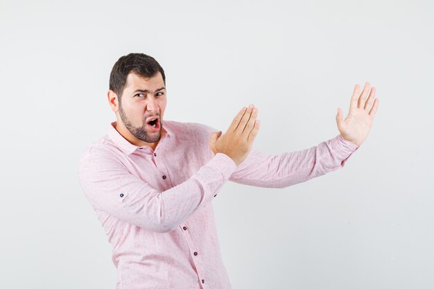 Młody człowiek w różowej koszuli pokazując gest cios karate i patrząc zły