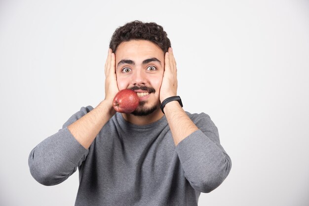 Młody człowiek w szarej bluzie trzymając jabłko w ustach.