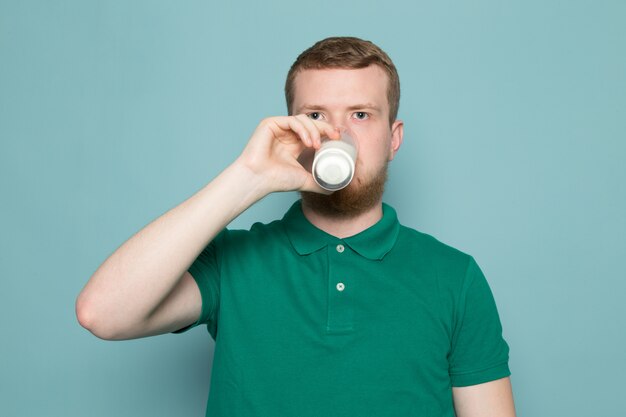 Młody człowiek w zielonej koszulce szklankę do picia z mlekiem